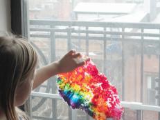 girl holding wax paper rainbow art against window