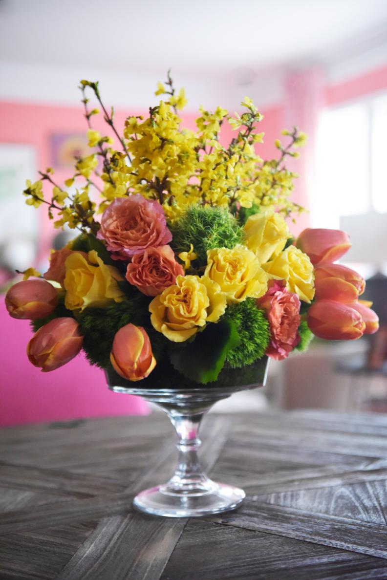Springtime doesnâ  t have to be all about pastels. Take the less expected approach to your centerpieces by sticking with citrus tones and creating a formal arrangement with a fresh mix of forsythia, parrot tulips, dianthus and roses.