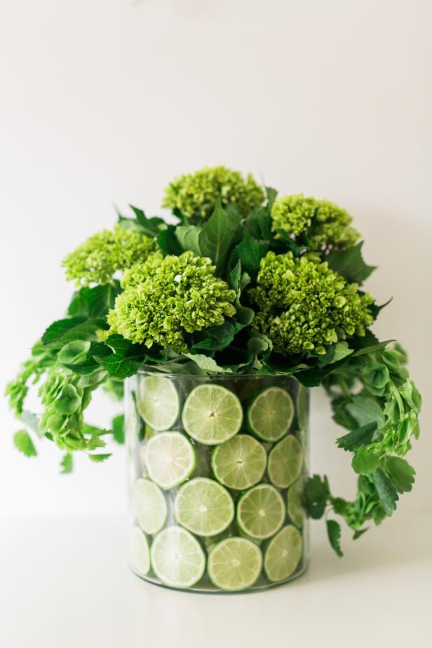 Bring a touch of citrus to your tabletop with an arrangement of fruit slices with vibrant flowers. Gather the following materials for this spring project: (4) limes, lemons or oranges per vessel, (1) 10-inch diameter round glass vessel, (1) 8-inch diameter round glass vessel, floral shears, floral wire, wire snips, paring knife, water, glass, cutting board, (2) bunches of bells of Ireland and (2) bunches of a coordinating green flowers.