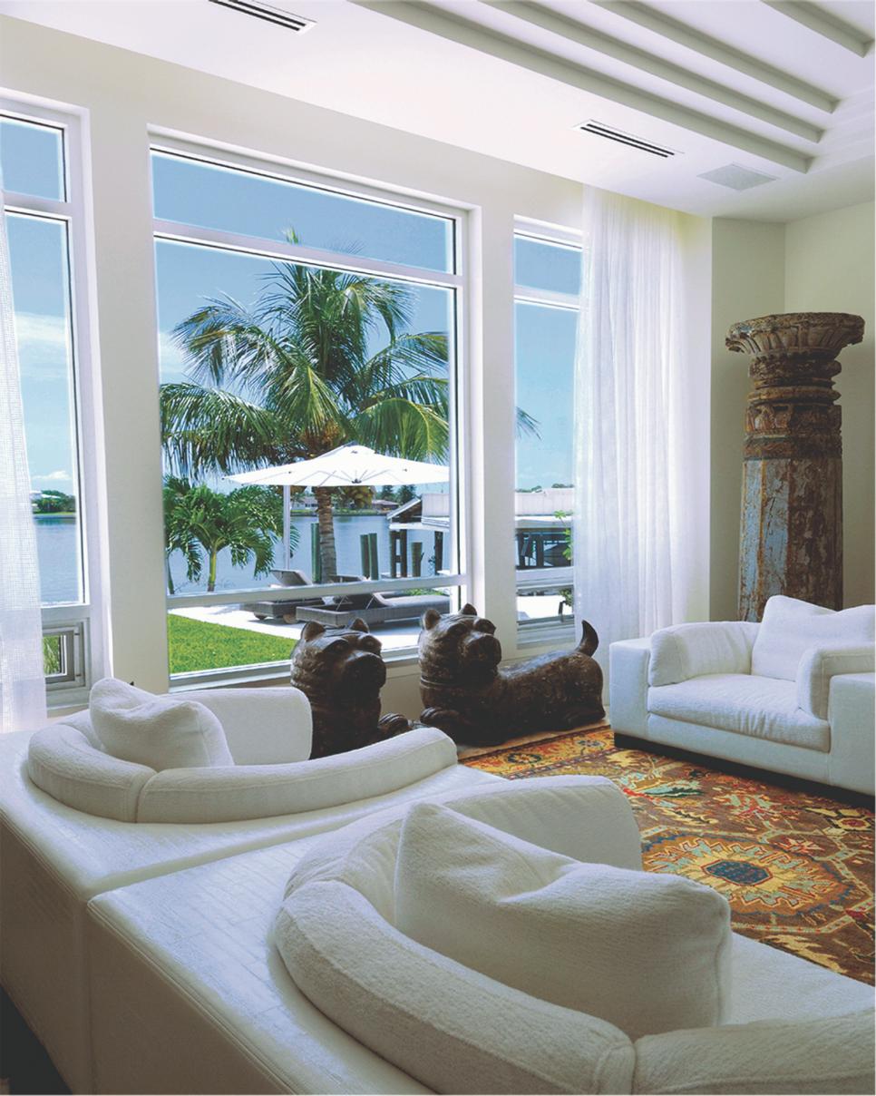 Eclectic Living Area Features Stunning Waterfront View Living Space With Floor-to-Ceiling Windows and White Armchairs