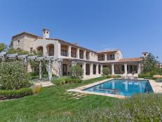 Back view of a French-inspired home with swimming pool and pergola.