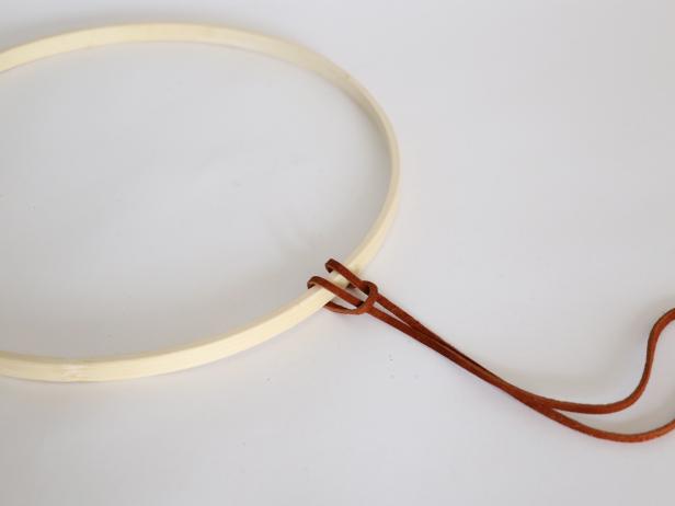 You’ll only be using the hoop that does not have the screw on it. Fold one leather strand in half, leaving the ends uneven. Thread the ends through the folded loop around the hoop creating an overhand knot. Pull tight.