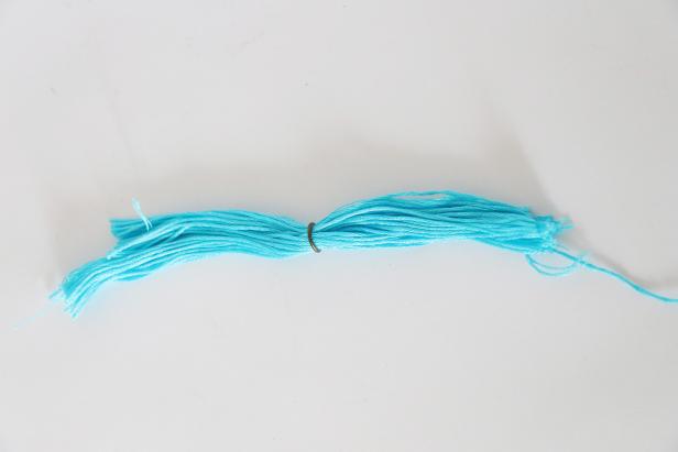 Unfold both halves. Put the embroidery floss through a small metal ring. Place the ring in the center of the floss.