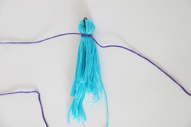 Fold the floss in half with the ring in the bend. Tie another color of floss underneath the ring. Wrap it around a few times and tie again. Cut off the extra ends.