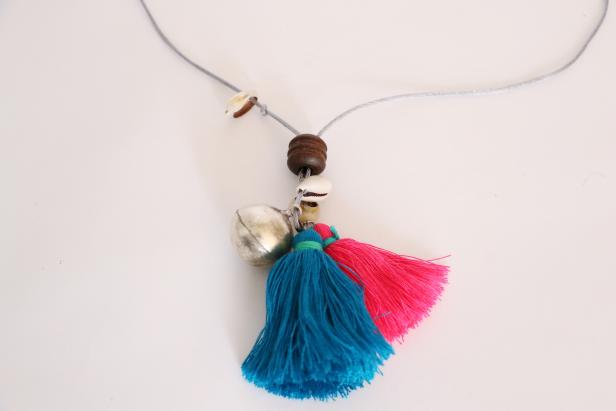 Thread everything that will be at the center of your necklace first. I used two tassels, two bells, and two shells. To keep all of these from moving around on your necklace, bring both ends of the cord up through one bead. This bead will hold everything in place.