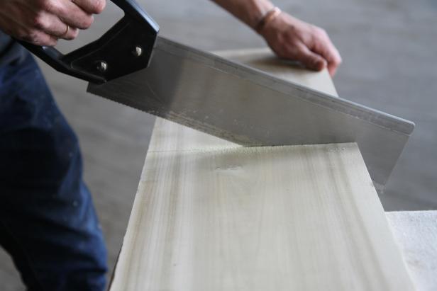 Cut poplar wood piece using a hand saw to make a cutting board.