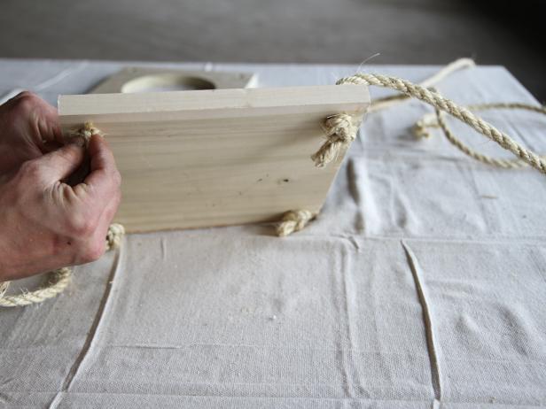Slide the first piece of wood through the ropes.