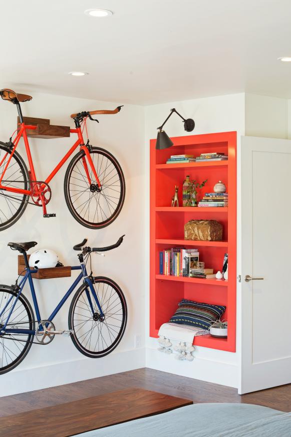 Bike Storage Is Functional and Decorative in Hip Bedroom White Bedroom With Bikes on Wall Racks and Red Built-In Bookcase