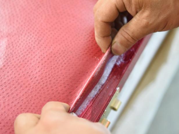 To attach fabric on the hinged side, pull the fabric across the batting and make a chalk line along the edge. With scissors, cut the fabric .5â outside that line to allow for some excess material. Then, fold that excess under and neatly staple along the door edge. Keep in mind, youâll want to avoid staples on any areas of the door that will not eventually feature nailhead trim.