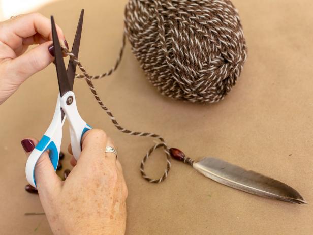 You may want to use the scissors to snip the ends of the feathers to make them thinner to make this step a bit easier. Thread an 18 inch piece of yarn through a wooden bead, using a yarn needle, if necessary. Leave about 3 inches at one end. Push 3 inches of yarn and bead onto the quill, with the short end of the yarn exposed near the feather. Tightly wrap the remaining yarn around the exposed quill and secure with hot glue. Cut yarn and set feathers aside.