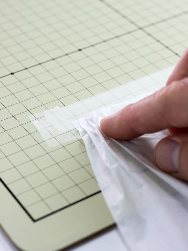 Cut a 7" x 20" piece of tissue paper. Attach the 20" side of the tissue paper to the upside-down tape strip by pressing 1/4" folds onto the adhesive, overlapping the folds as you go.