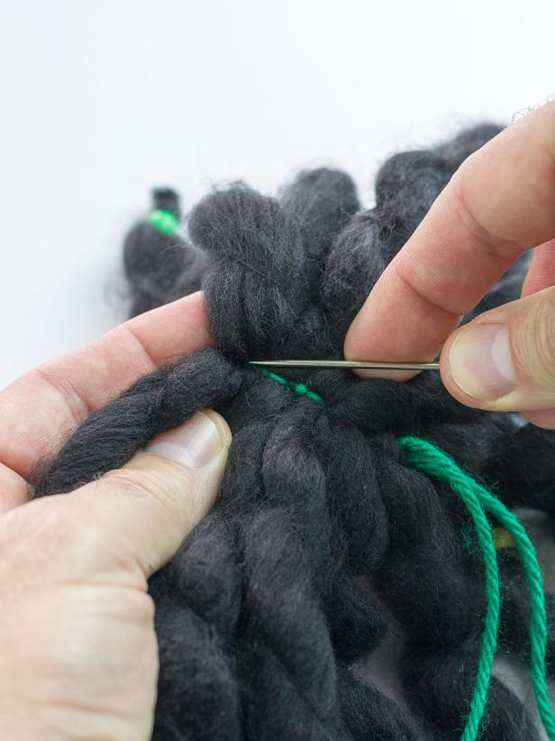 Thread one of the green yarn ends through the needle and stitch it into the opposite end of the grouped lengths.You should now have one end of the green yarn on either side of the dreadlocks.