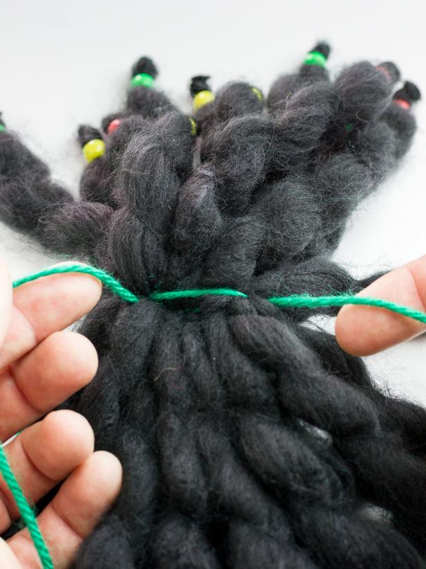 Thread one of the green yarn ends through the needle and stitch it into the opposite end of the grouped lengths.You should now have one end of the green yarn on either side of the dreadlocks.