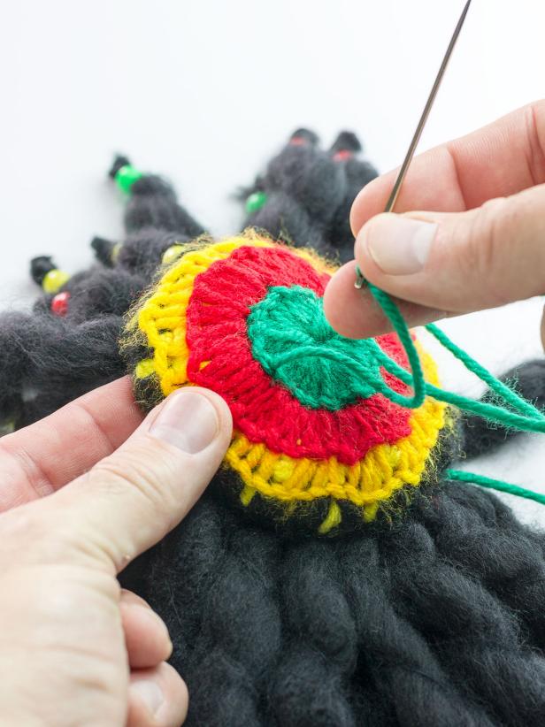 Use the threaded needle to stitch the center of the dreadlocks to one side of the hat’s green center. Remove yarn from needle and thread opposite end of green yarn from dreadlocks through needle before repeating this process, stitching it to the opposite side of the hat's green center so the 'hair' is securely attached to the hat.