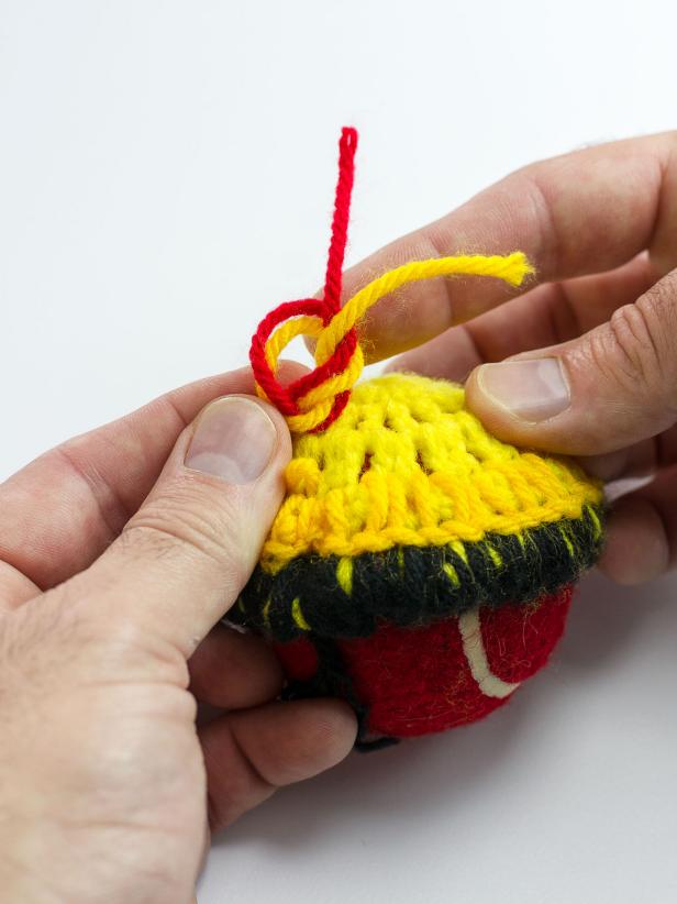 Tie yellow yarn to the end of the black yarn, knotting it very close to the doily. Continue stitching around the second circle of the doily with yellow yarn. When you reach the end of the circle, tie red yarn to the yellow yarn keeping the knot very close to the doily.