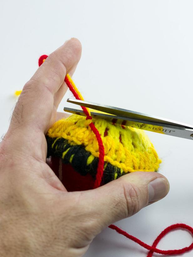 Tie yellow yarn to the end of the black yarn, knotting it very close to the doily. Continue stitching around the second circle of the doily with yellow yarn. When you reach the end of the circle, tie red yarn to the yellow yarn keeping the knot very close to the doily. Cut off any excess.