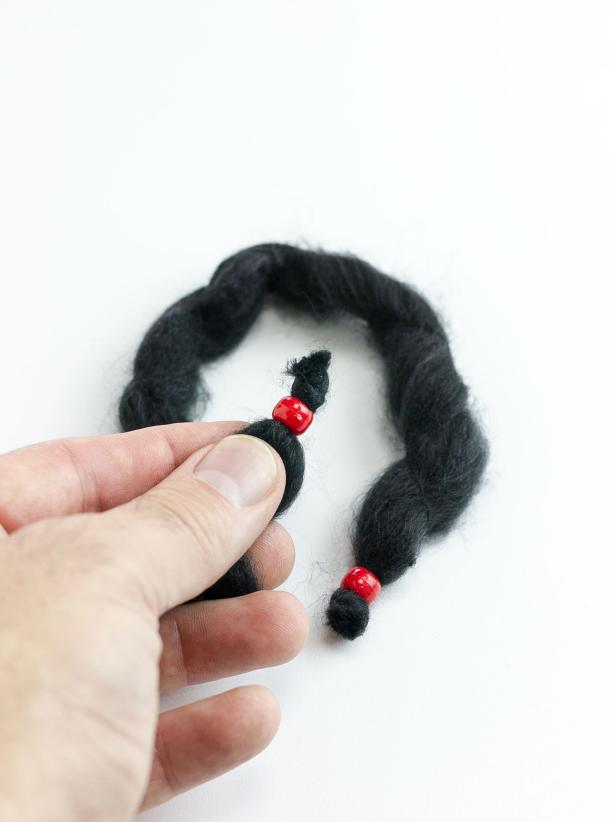 Cut the chunky black yarn into 12 varying lengths between 7 and 9 inches. Thread a pony bead onto the ends of each length and tie a knot in the yarns' ends to secure the beads.
