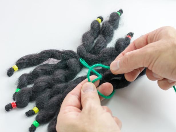 With all 12 lengths of chunky yarn laying side-by-side, use a piece of yarn to knot them together while still keeping them side-by-side.