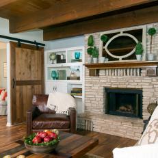 Sliding Wood Barn Door in Cozy Country Living Room With Textured Fireplace Surround and Leather Armchair 
