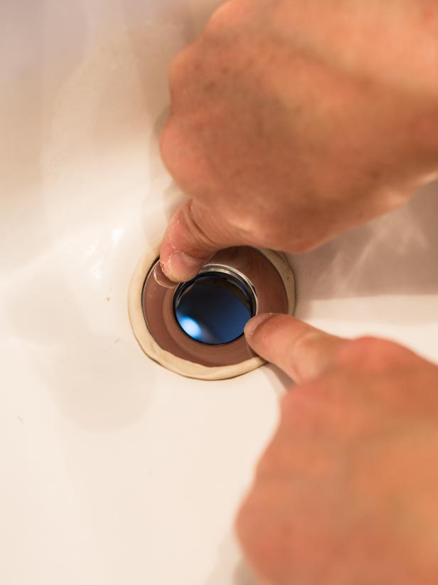 Roll a small wad of plumberâs putty between hands into a âsnakeâ thatâs long enough to reach around circumference of the drain hole. Press into place around the drain hole in sink. Push rubber seal and top of drain (flange) firmly into ring of putty. Install drain body up through sink opening and reattach the flange (inside sink) to drain opening and body (under sink). Turn flange (inside sink), until finger tight. Hold drain body in place, with pivot rod opening (for plugging drain) facing back of the sink, and tighten mounting nut (just under sink) with channel lock pliers. Tightening the drain will cause plumberâs putty to squeeze out. Pull away excess with fingers.