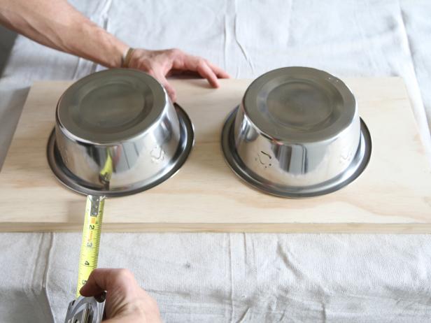 Place two stainless pet feeding bowls upside down on the wood stair tread, and measure to space them evenly.