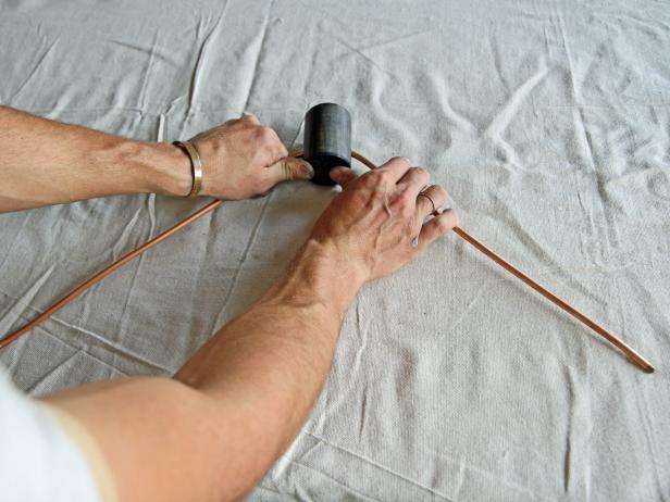 Slowly bend each side of the copper pipe down away from the dowel, creating a triangular shape.