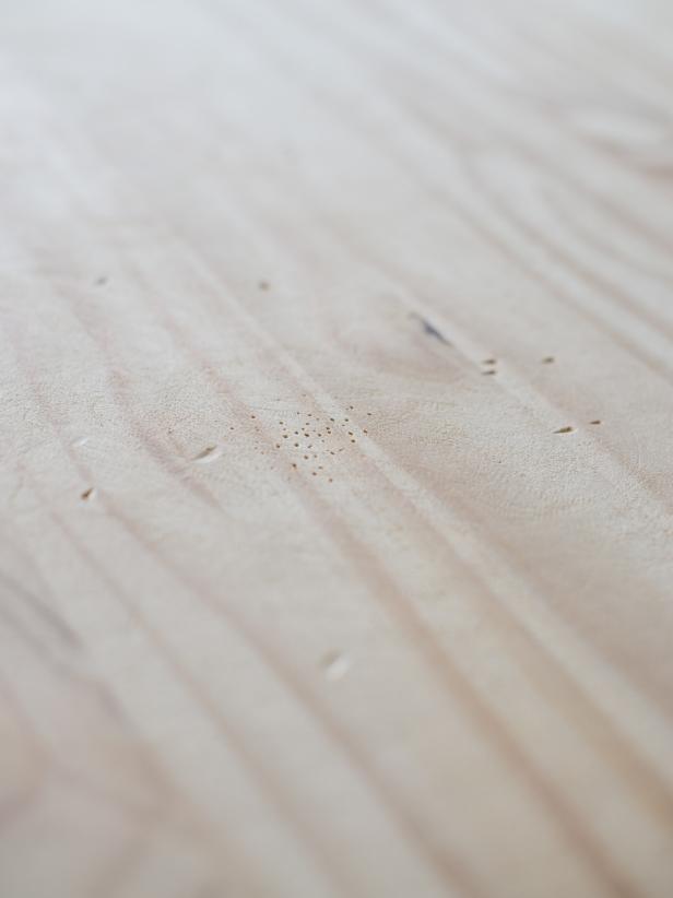 Start with raw wood tabletop. Old finishes can be stripped or sanded off prior to this step. Use hammer, nails, screws and/or metal chair to beat and distress surface of the wood. These marks, dents and dings should be somewhat random. Tip: A nail point can be used to create a cluster of “worm holes” to give the wood more character.
