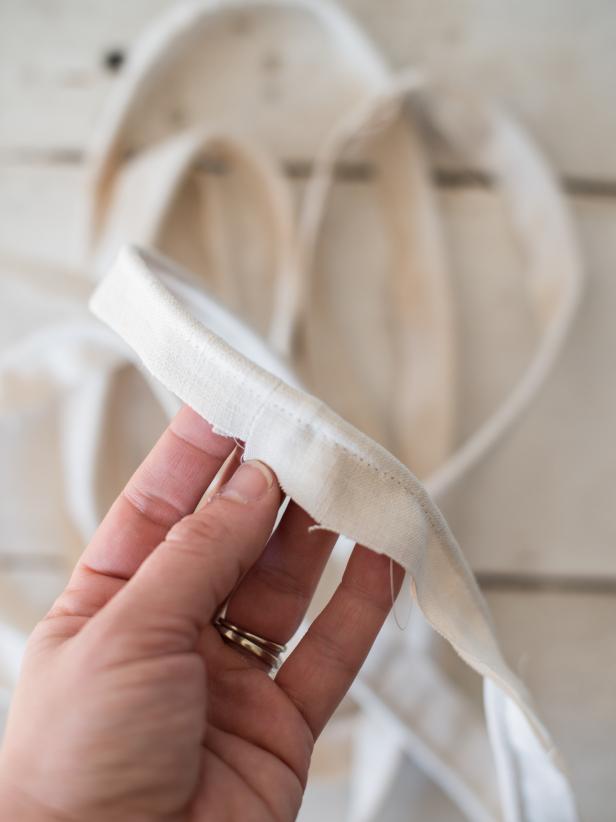 To figure out how much cotton cording is needed for this project, measure circumference/perimeter of ottoman and then double that measurement, so there is enough piping for the top and bottom of ottoman side. Cut length of cotton cording to measurement. Cut the same length of fabric in 3” wide strips to use to cover cotton cording. These fabric strips should be cut at an angle or “on the bias”, so it lies flat when sewn. If necessary, sew shorter pieces together to have lengths long enough to cover cotton cording. Press seams open with an iron, so they lie flat. Wrap fabric around cotton cording and sew into place with a sewing machine equipped with a zipper foot.