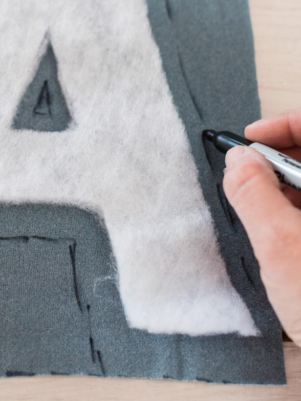 Use cut batting as template to trace each letter onto fabric, leaving a 1/2″ border to pull around sides of the letter in order to staple it in place. Make sure fabric is face down, so the letter is being traced in reverse. This way, the letter will be facing the proper way once it’s flipped over. For letters with a hole in the middle, cut small hole and a few small slits that will allow fabric to be pulled through. On a flat work surface, layer each letter fabric first, face down, followed by quilt batting and then the chipboard letter.