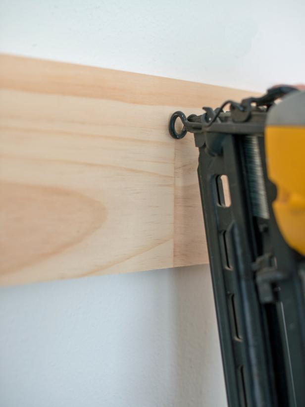 Cut 1” x 6” board to proper width for wall. Hold in place, lining bottom edge up with pencil mark. Balance a level on top and adjust until bubble shows board is level. Nail into place with 1 ¼” finish nails. Place two nails, one towards top and one towards the bottom of the board, every 10-12”. It is best if a few nails securing each board are shot into studs. Use a stud finder and mark their location lightly with a pencil while working around the room. Tip: Start on the least visible wall in the room, so your technique can be perfected before working on areas that are focal points.