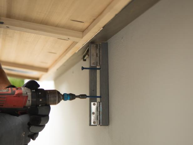 Prop up the bar or have a friend lift the bar top up and using the same method in the previous step, secure the three brackets to the house, making sure they line up with the 1”x2” braces on the underside of the bar. Begin by installing the center bracket first, then swing it out to hold the bar up as you work and install the side brackets.