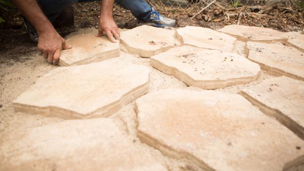 Continue placing pavers, checking that they’re level as you work and leaving somewhat uniform gaps between the stones. As you get close to the perimeter, choose smaller stones and turn appropriately so you don’t overstep the patio’s border