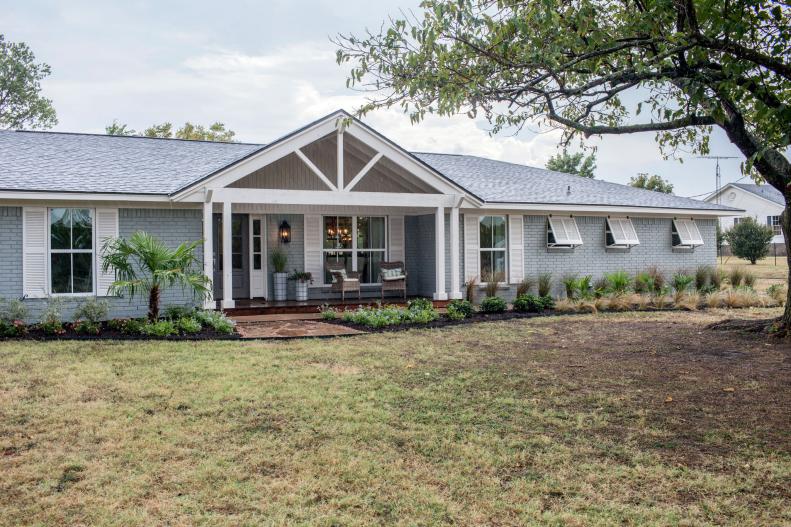The exterior of the Ermoian remodeled home has new white shutters, a fresh landscape, a grey brick tone and white pillars shaping their front porch, as seen on Fixer Upper.
