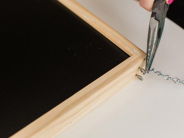 Using pliers, pry open the end links on both sections of jack chain. Take one chain’s ends and connect it to the screw eyes on the right side of the chalkboard. Repeat this on the left side.