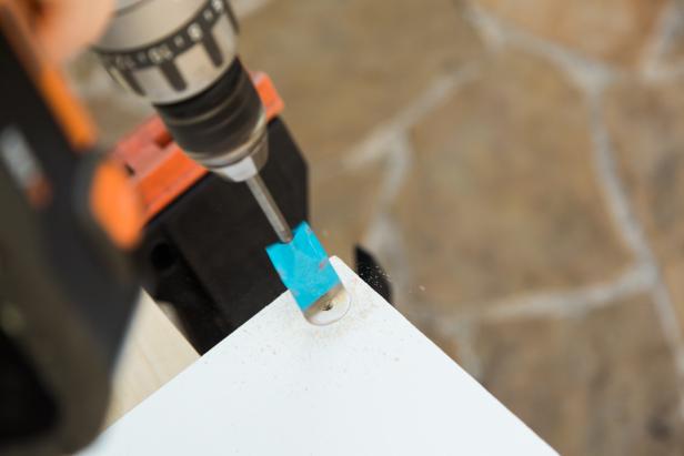 Next, prepare the 1” spade bit with some painters tape to act as a depth guide so you don’t drill too deep into the bottom side of each shelf. You want to drill just deep enough so that each plastic grommet fits flush and is hidden from view. Tape the bit so that just 3/8” of the tip is exposed. Line up the point of the spade bit with your pencil mark and drill down slowly so you don’t go too deep. Your bit’s sharp tip will go through a little bit on the other side but that’s OK. Repeat until all 12 holes are prepped. HINT- once you’re done, resist the urge to stick a grommet in there at this point, as it may get stuck