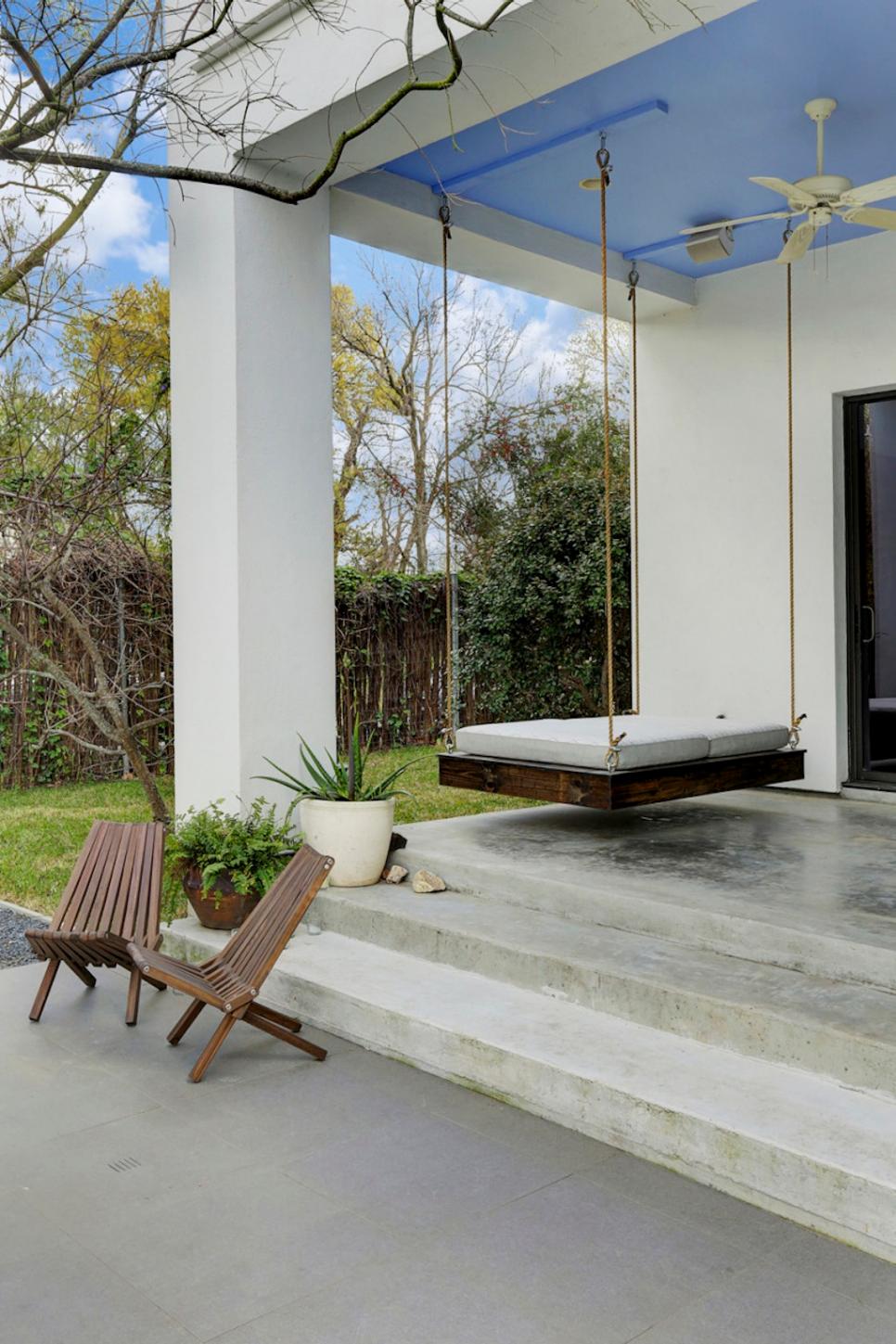 Covered Porch With Blue Painted Ceiling Over Hanging Bed Swing and Concrete Steps Leading to Wooden Outdoor Chairs Contemporary Covered Porch