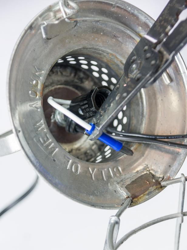 Feed the cut cord through the finial on the outside of the lantern hood into the inside of the hood. Pull about 6 inches of the cord through. Tie a knot in the cord close to the lamp rod. Split the end of the cord and remove about ½â of coating from both sides. Remove ½â of the coating from the socket wires. Twist all of the ends tightly between your fingers. Insert one of the cord wires in an electrical connector and crimp the connector tightly around the wire with wire cutters. Insert one of the socket wires in the opposite end of the electrical connector and crimp. Repeat for the other wires. Tuck the connected wires up in the lantern hood.