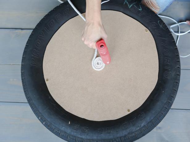 Starting on the top center of the circle, glue the clothesline in a tight spiral. Use a good amount of glue and try to not leave any gaps between the rope. Keep adding rope until it reaches the edge and continue down the sides of the tire. Flip the tire over and add rope until you cover the bottom side.