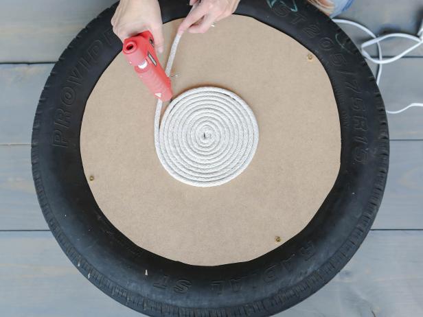 Starting on the top center of the circle, glue the clothesline in a tight spiral. Use a good amount of glue and try to not leave any gaps between the rope. Keep adding rope until it reaches the edge and continue down the sides of the tire. Flip the tire over and add rope until you cover the bottom side.
