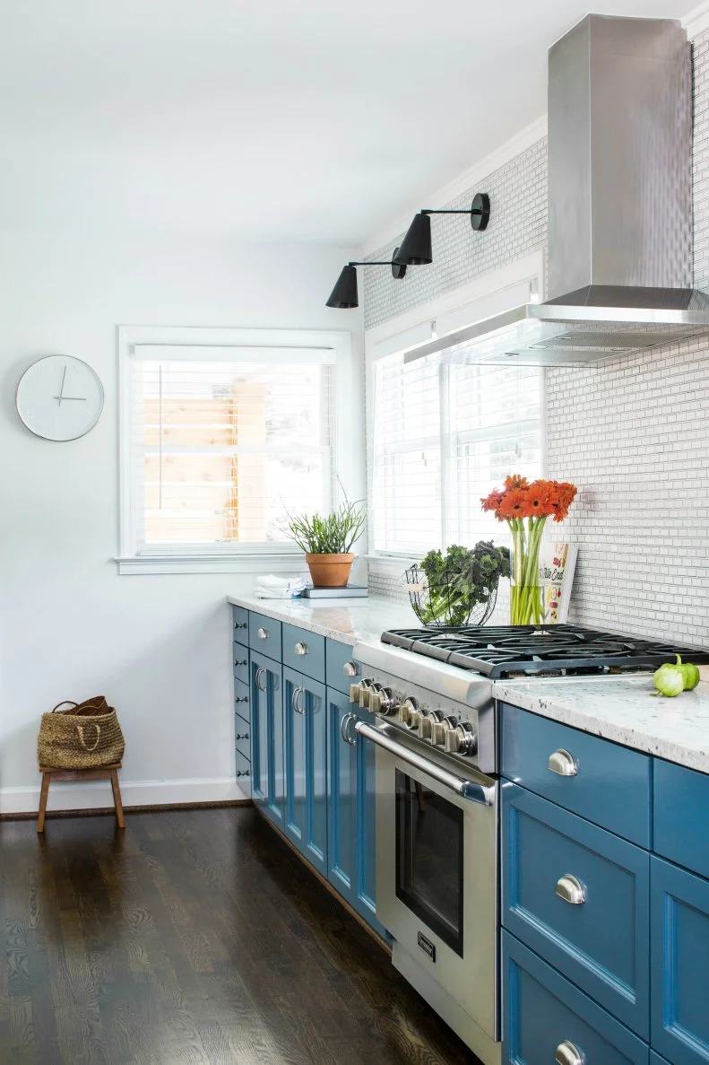 Modern White and Blue Kitchen with Metal Vent Hood, Tile Backsplash and Simple Sconces and Clock
