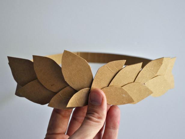 Cut open cereal box. Cut one long strip of cardboard and 20-25 leaves. Take cardboard strip and hold around head of the costume wearer to gauge size. Cut to length and use hot glue gun to glue ends together to create a headband. Hot glue leaves onto front half of the headband. Spray paint wreath gold.