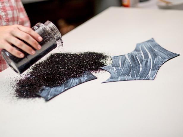 Lay out two sheets of 9x12 black foam sheets together. Draw an outline of the wings and ears for the bat pumpkins. Use your scissors to cut along the outline of the wings and ears from the black foam. While the glue is still wet make sure to pour a significant amount of glitter to fully cover the surface. Let dry and then carefully shake off the excess glitter.