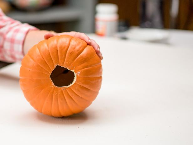 Set the larger pumpkin aside and lay the smaller pumpkin on its side. Trace around the outside of the plastic vampire teeth with a marker near the center of the small faux pumpkin.  Cut along your marker line with the pumpkin carving knife to create a place for the plastic vampire teeth.  Remove the excess piece and turn the bottom of the pumpkin towards you for cutting.  Insert the pumpkin carving knife into the bottom of the small faux pumpkin and cut about a 3 inch circle. Tip: This will not have to be a perfect circle. The circle just needs to be wide enough for the larger pumpkin top to go inside the smaller pumpkin bottom and be secured with hot glue.