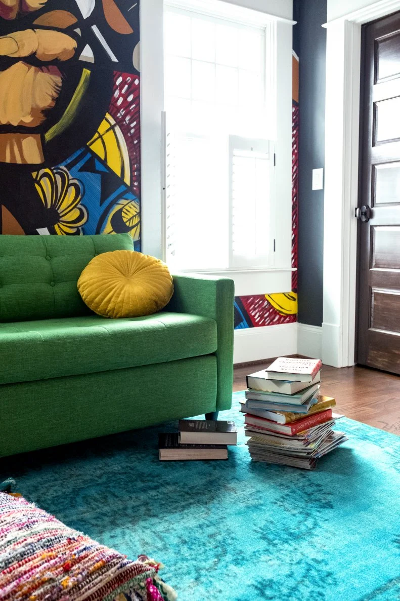 Stack of books next to green sofa infront of Graffiti wall.