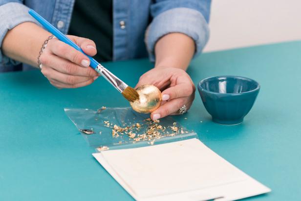 Roll the plastic egg in the gold leaf sheet (metal leaf adhesive dries tacky). Smooth out gold leaf with the paintbrush.