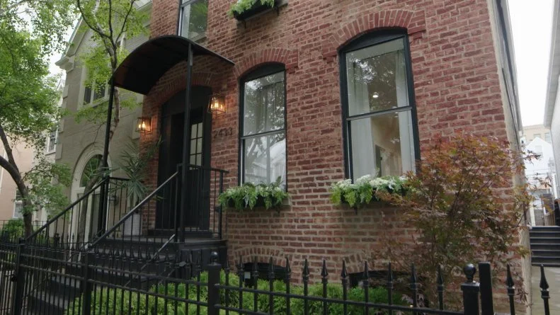 The completed exterior of the Lincoln Park Fourplex remodeled on Windy City Rehab features a refinsihed entrance with a stylish black arch, brand new black framed windows, charming window boxes, and lush new landscaping.