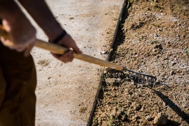 Rake soil level and ensure that it’s one inch below the grade of sprinkler heads or paved areas, like sidewalks, patios or driveways. Raking evens out the surface and also creates loose soil particles, which are ideal for grass roots to sink into.