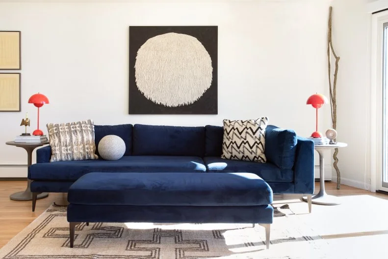 The open plan living room is grounded by a refined color palette of navy blue, black and pops of red. Over the sofa, a painting of a lion mane’s mushroom adds a modern, rustic touch to the living area. The mushroom silhouette continues with two bright Verner Panton Flowerpot Lamps. The table lamps bring a 1960s vibe into this modern living room. 