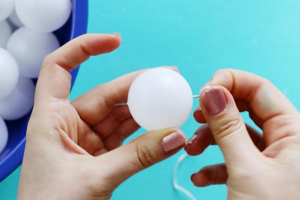 Then, push the needle through the ping pong ball, using a jar grip to help pull it through the other side.