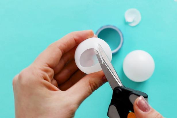 Begin by cutting a circle in the top and bottom of one ping pong ball. Then, use hot glue to glue it on top of another ping pong ball.